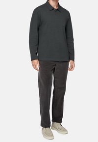 Tmavě zelená polo košile s dlouhým rukávem, límečkem a kapsou, v kombinaci s tmavě šedými kordovými kalhotami a béžov ými nazouvacími botami.