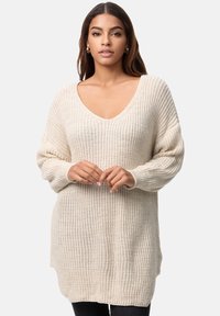Beige Chunky-Strickpullover mit tiefem V-Ausschnitt, langen Ärmeln, gerippten Bündchen und seitlichen Schlitzen. Der Stoff ist strukturiert und weich.