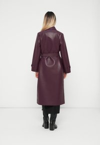 Long, purple faux leather trench coat with a belted waist, buttoned cuffs, and a smooth, glossy texture, featuring a mid-calf length.