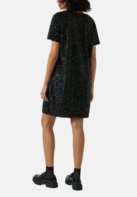 Czarna sukienka z cekinami, z krótkimi rękawami i luźnym krojem, z okrągłym dekoltem. Noszona z masywnymi czarnymi butami na platformie.