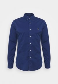 Tmavě modrá košile s dlouhým rukávem na knoflíky z bavlny, s klasickým límečkem a malým žlutým vyšívaným logem na hrudi.