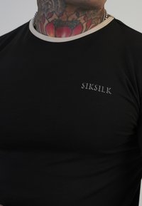 Must must shirt beežide servadega kaelusega, millel on rinna peal valge tikandiga logo "SIKSILK", valmistatud siledast kangast.