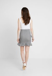 Gonna a quadretti bianchi e neri con orlo arricciato, lunghezza metà coscia e vita con cintura. Abbinata a una blusa senza maniche bianca e scarpe.