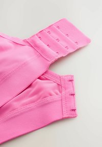 Roze sportbeha van zacht materiaal, met verstelbare schouderbanden en haak-en-oogsluiting. Heeft een mesh voering voor ademend vermogen en naadloze randen.