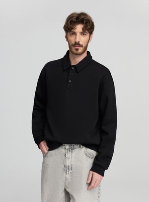 Polo nera a maniche lunghe con tre bottoni, polsini a coste e una texture morbida, abbinata a jeans di denim grigio chiaro con motivo.