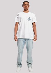 White cotton t-shirt with a crew neckline, featuring a navy blue "University Soccer Club" graphic on the left chest. Light blue jeans, white sneakers.