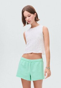 Bílý, strukturovaný crop top s okraji bez obšití, spárovaný se světle zelenými šortkami na šňůrku s třepeným lemem. Jednoduchý, ležérní outfit.