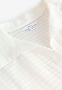 Chemise blanche à col avec de fines rayures verticales et une étiquette de la marque « NEXT » à l'intérieur de l'encolure.