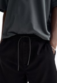 Pantalon noir coupe décontractée avec une ceinture élastique et un cordon gris, assorti à un t-shirt gris foncé en matière douce.
