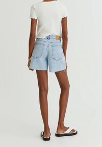 Shorts en jean bleu clair avec ourlet effiloché, deux poches arrière et taille haute. Associés à un haut blanc côtelé à manches courtes et des sandales noires.