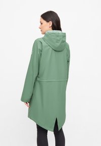 Grön vattentät jacka med huva, med ett kontrasterande mönstrat foder, långa ärmar och en bakre ventil för ökad luftcirkulation.