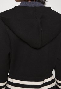 Schwarzer Strick-Hoodie mit einer großen Kapuze, ausgestattet mit weißen und marineblauen horizontalen Streifen am Saum für Kontrast und Struktur.