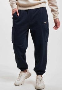 Pantaloni jogger navy realizzati in morbido tessuto, dotati di tasche laterali, inserti in tessuto a costine sui lati e polsini elastici alle caviglie.