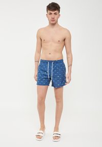 Pantaloni da bagno blu con un motivo di piccoli pesci verdi e azzurri, vita con coulisse, dalla texture liscia e lunghezza a metà coscia.