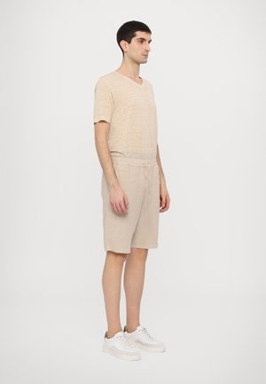 Beige linned t-shirt med v-hals, parret med lysebeige shorts og hvide sneakers. Stoffet har et tekstureret og åndbart udseende.