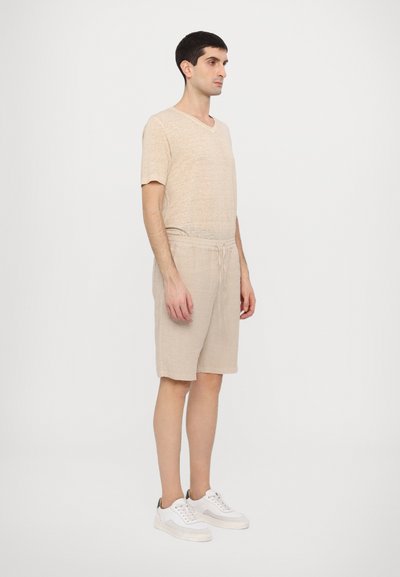 Beige linen t-shirt with a v-neck, paired with light beige shorts, and white sneakers. The fabric has a textured, breathable appearance.
