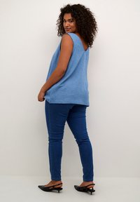 Top in tessuto blu intrecciato con scollatura ampia e retro a V, abbinato a jeans skinny blu e mule neri con design slingback.