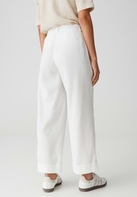White loose-fitting trousers with a cuffed hem, elastic waistband, and two back pockets, paired with light-colored sneakers.
