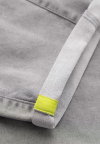 Gros plan sur un tissu gris plié avec une sangle texturée comportant une bande jaune cousue sur un fond gris.
