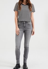 Pruhované černobílé tričko, přiléhavé šedé džíny, kotníkové boty a hladká textura. Džíny mají vysoký pas a slim fit.