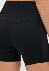 Calções pretos de cintura alta feitos de material elástico, com costuras flatlock, uma textura suave e bolsos laterais para funcionalidade.