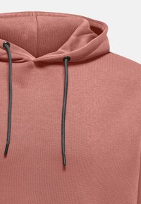 Rosa hoodie med en blød tekstur, featuring en snor med sorte spidser og et afslappet hætte-design. Simpel, minimalistisk stil.