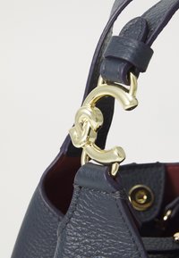 Marine lederen handtas met een gestructureerd oppervlak, voorzien van een gouden kettinglink en hardware. Het interieur heeft een contrasterende rode voering.