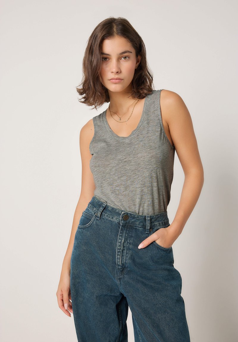 Siv brezrokavnik z izrezom v obliki črke U, kombiniran z visokim pasom temno modrih kavbojk s stranskimi žepi in rahlo zbledelo teksturo.