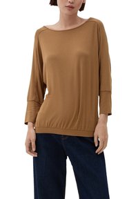 Brązowa, długa bluzka z okrągłym dekoltem i marszczonym dołem. Gładki, elastyczny materiał. Noszona z ciemnymi dżinsami.