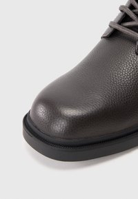 Botă din piele gri închis, cu un finisaj texturat, vârf rotund și talpă din cauciuc negru. Prezintă șireturi și detalii de cusătură în ton.