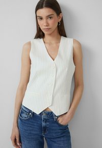 Weißes, gestreiftes Weste mit V-Ausschnitt, fünf Knöpfen und Taschendetails, kombiniert mit blauen Jeans. Glatte, maßgeschneiderte Passform.