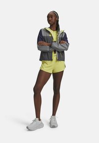 Gray and navy color-blocked windbreaker with a hood, paired with a bright yellow athletic top and shorts, and light gray sneakers.
