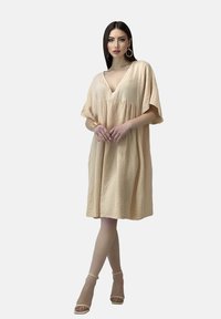 Pfirsichfarbene, knielange Kleid aus strukturiertem Stoff mit einem V-Ausschnitt und kurzen Ärmeln, in einer lockeren, fließenden Silhouette.