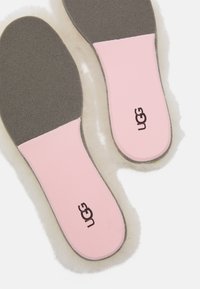 Roze i sivi ulošci s teksturiranom ružičastom površinom i mekanim rubom, s UGG logotipom. Mekani materijali osmišljeni za udobnost.