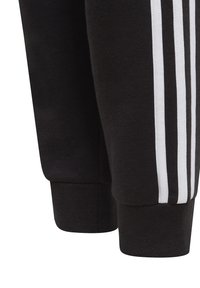 Pantalones de chándal negros hechos de material suave, con tres rayas blancas a lo largo de los lados y puños acanalados en los tobillos.