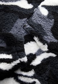Couverture en polaire présentant un motif abstrait monochrome en noir, gris et blanc. Texture douce avec une finition moelleuse.
