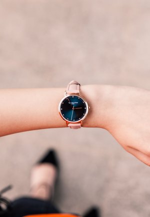 Orologio oro rosa con quadrante rotondo sfumato blu, cinturino in silicone rosa chiaro e indici delle ore minimalisti in argento. Dettagli di design classico visibili.