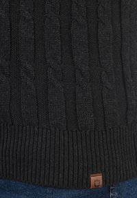 Schwarzer Kabelstrickpullover mit einem strukturierten Muster und geripptem Saum. Ein kleines Lederetikett ist an der Unterseite angebracht.