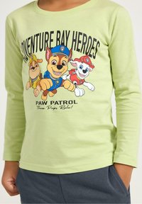 Groen shirt met lange mouwen met de tekst "Adventure Bay Heroes" en cartoon honden. Zachte katoen, ronde halslijn en geribbelde manchetten.