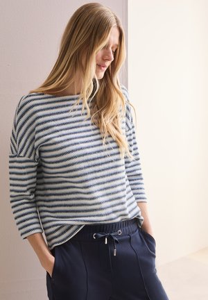 Pull rayé bleu et blanc avec un col bateau et des manches trois-quarts, associé à un pantalon marine foncé avec une taille à cordon.