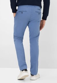 Lichtblauwe katoen broek met een slim fit, voorzien van twee achterzakken met knopen en gedragen met witte sneakers.
