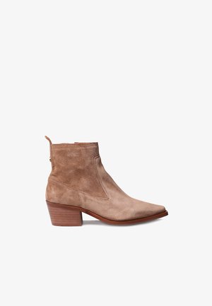 Bottine en suede beige avec un bout pointu et un talon empilé. Comprend des coutures latérales, une languette et une semelle en cuir lisse.