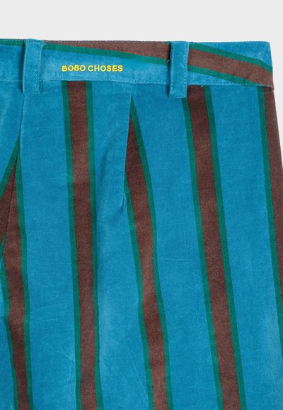 Svijetloplave platnene hlače sa vertikalnim prugama u tamnosmeđoj i zelenoj boji. Imaju oznaku s natpisom "BOBO CHOSES" u žutom. Glatka tekstura.