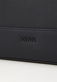 Svart lærveske med subtil søm, glatt tekstur, og en preget "JOOP!" logo på framsiden. Kompakt rektangulær form.