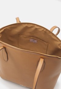 Sac à main en cuir fauve avec fermeture éclair, intérieur spacieux et une seule poche intérieure. Équipé de deux anses plates et d'une texture lisse.