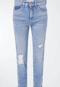 Jean bleu clair taille haute avec bouton et fermeture éclair, présentant des zones usées au genou gauche et à la cuisse droite.