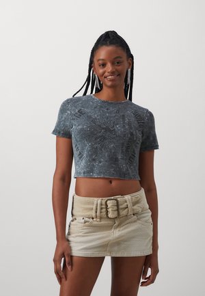 Cropped, dark gray T-shirt with a textured print and short sleeves. Paired with a beige corduroy mini skirt featuring a wide buckle belt.