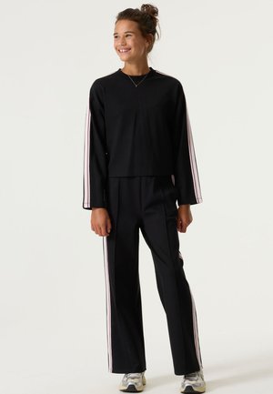 Zwarte cropped longsleeve top met roze zijkanten, gecombineerd met zwarte broeken met bijpassende stripes. Gladde, zachte stof.