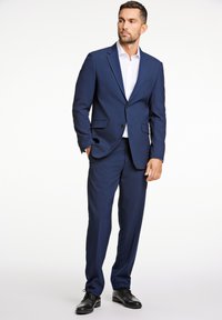 Traje azul marino con un corte ajustado, chaqueta de un botón, solapa y dos bolsillos frontales. Combinado con una camisa de vestir blanca y zapatos negros.