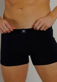 Boxer in cotone nero realizzati in tessuto elastico. Presentano un design aderente, una vita elastica con logo e una texture liscia.